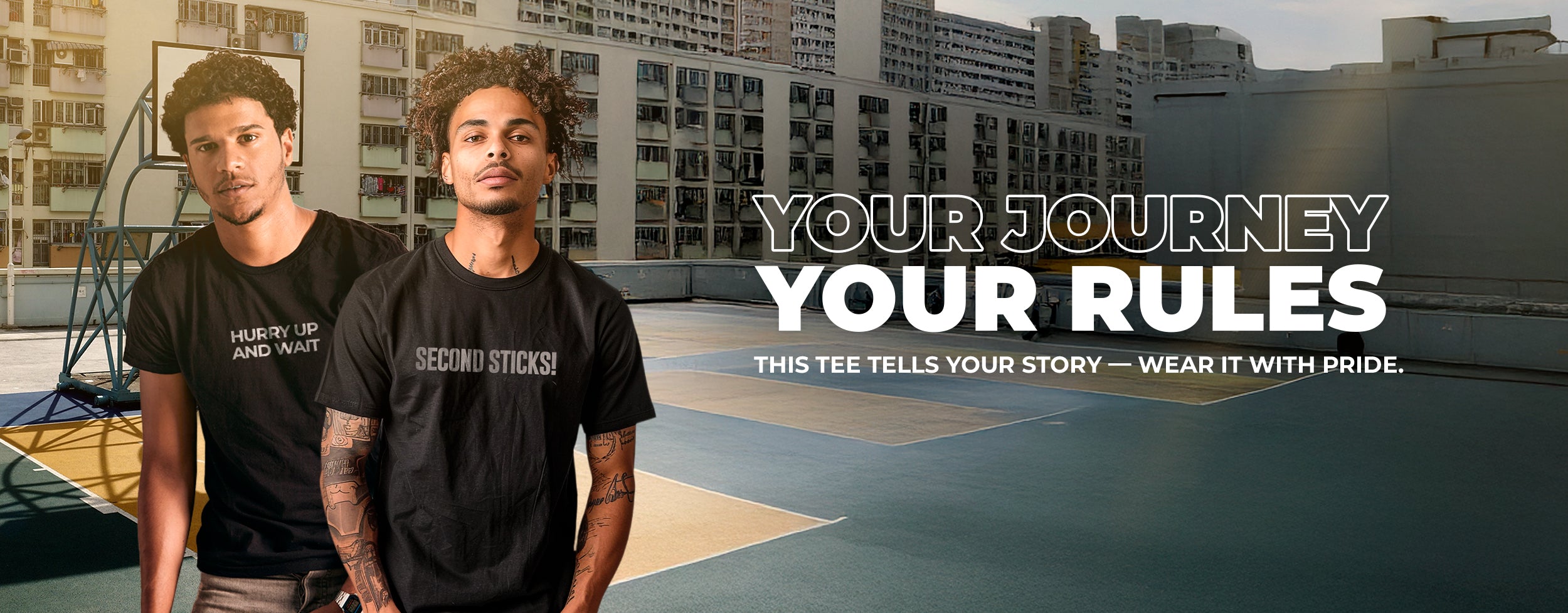 Two male models wearing Beard and Hat Actor black cotton t-shirts with film set quotes “Hurry Up and Wait” and “Second Sticks!” printed in gray, standing on an outdoor basketball court. Lifestyle fashion photography highlighting Beard and Hat Actor streetwear collection
