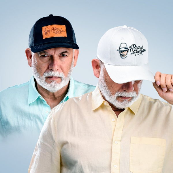 Male model wearing a white 100% cotton Beard and Hat Actor baseball cap with the original logo embroidered on the front. Behind him, another male model is wearing a black and gray trucker hat featuring a leather patch with the Beard and Hat Actor logo. Both models are styled in pastel shirts against a soft gradient background, showcasing the cap collection