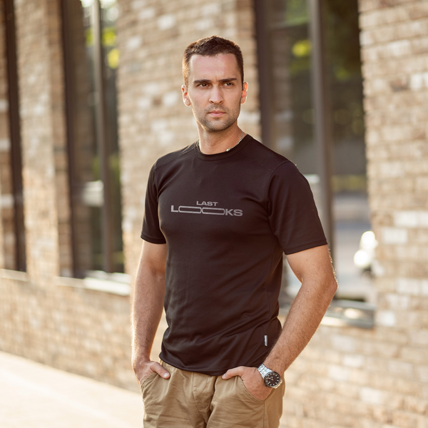 Male model wearing a black 100% cotton t-shirt from Beard and Hat Actor featuring the phrase “LAST LOOKS” printed in light gray