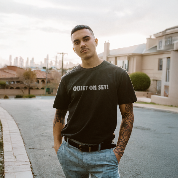 Male model wearing a black 100% cotton t-shirt from Beard and Hat Actor featuring the phrase “QUIET ON SET” printed in light gray